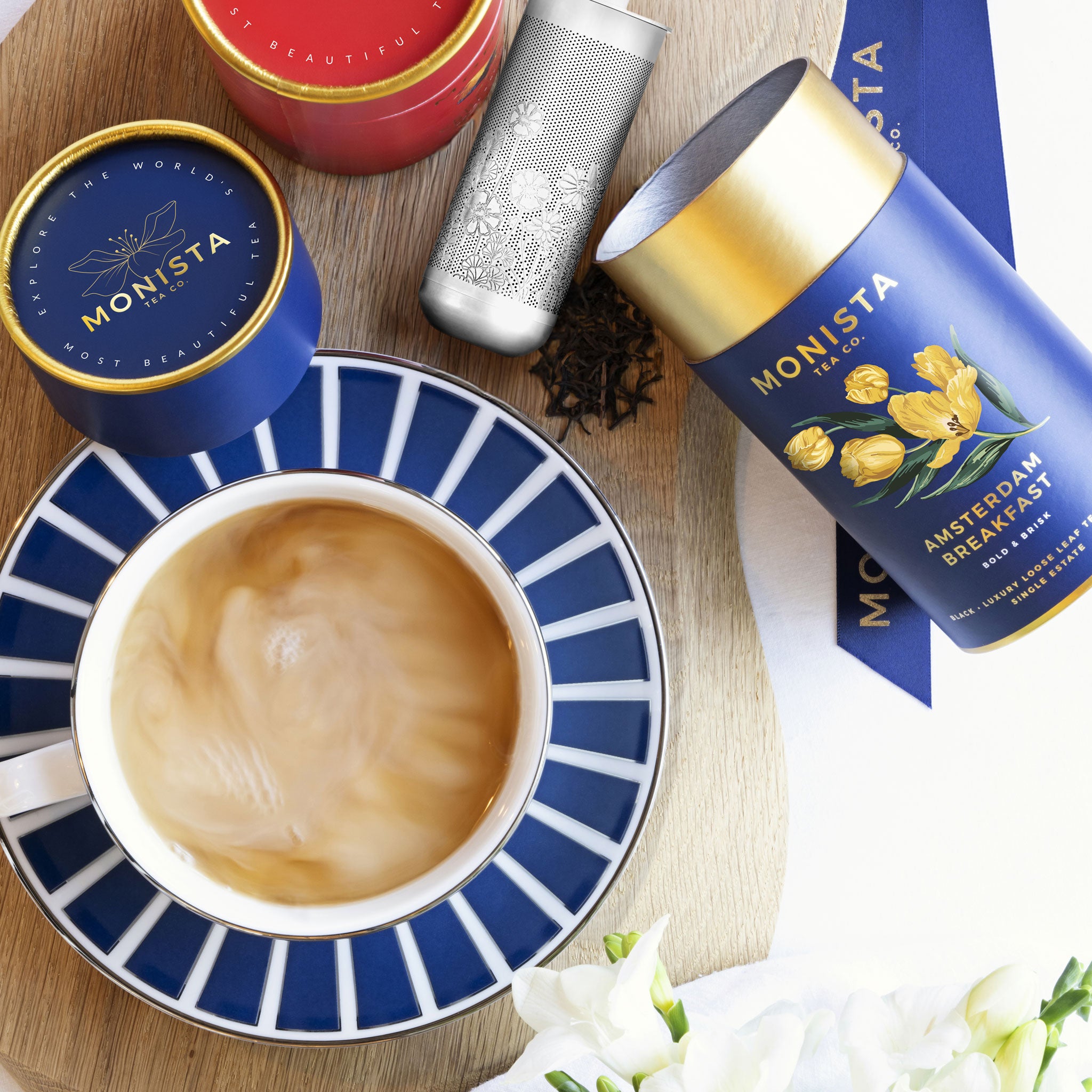 Cup of coffee with Monista tea canisters and packaging on a wooden surface.
