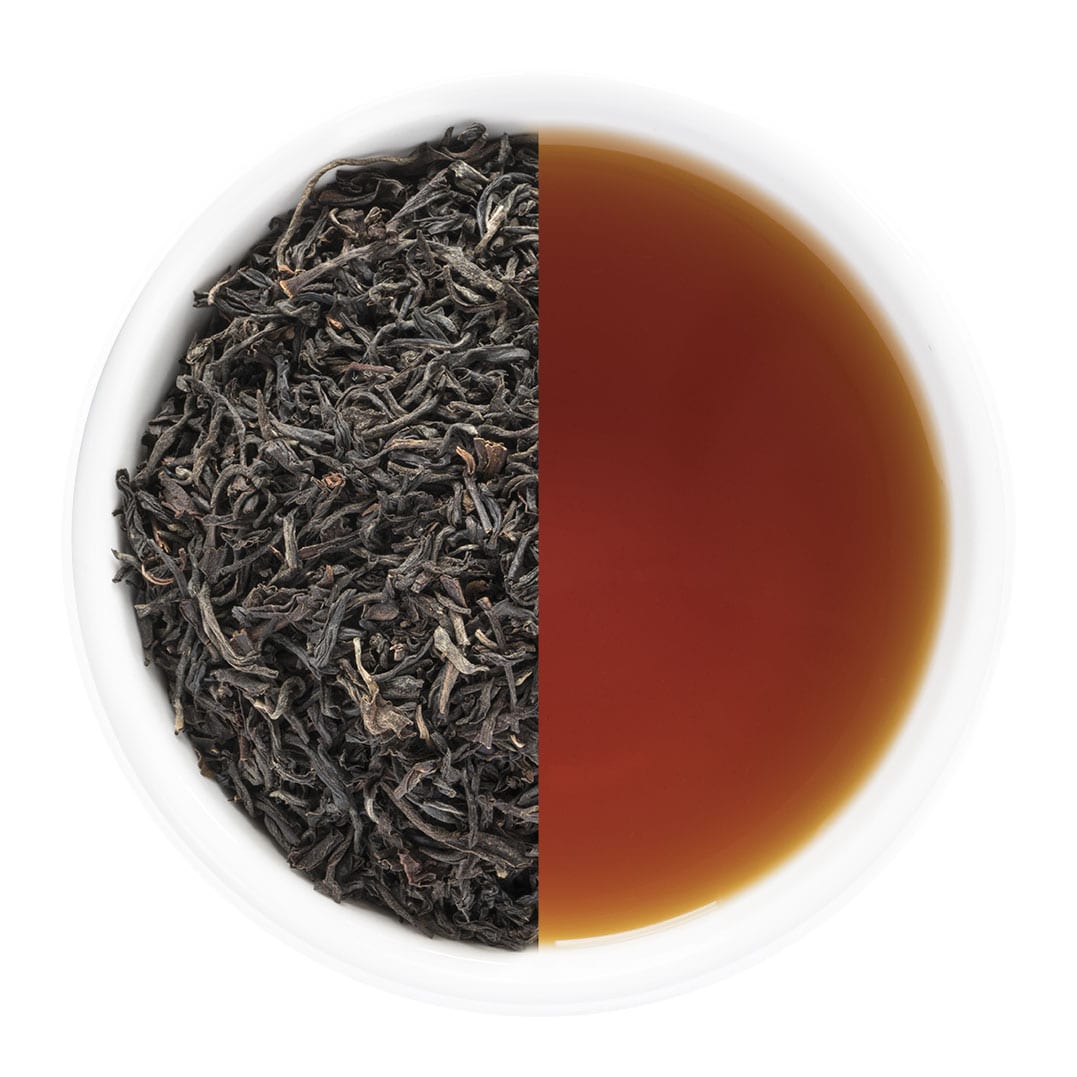 Tea leaves on one side and brewed tea on the other in a white bowl