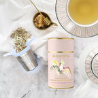 Monista tea canister with tea leaves, honey, and a teacup on a marble surface
