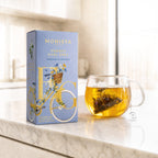 French Earl Grey pyramid tea bag box next to a glass mug of brewed tea with a tea bag steeping
