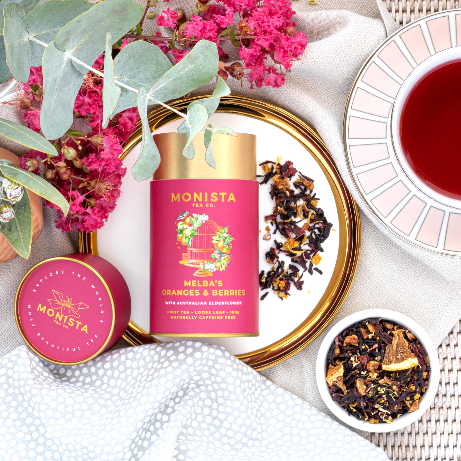 Monista tea packaging with flowers and tea leaves on a white surface
