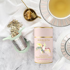 Mint green tea infuser with lemongrass and ginger tea, honey, and a cup of tea on a marble surface