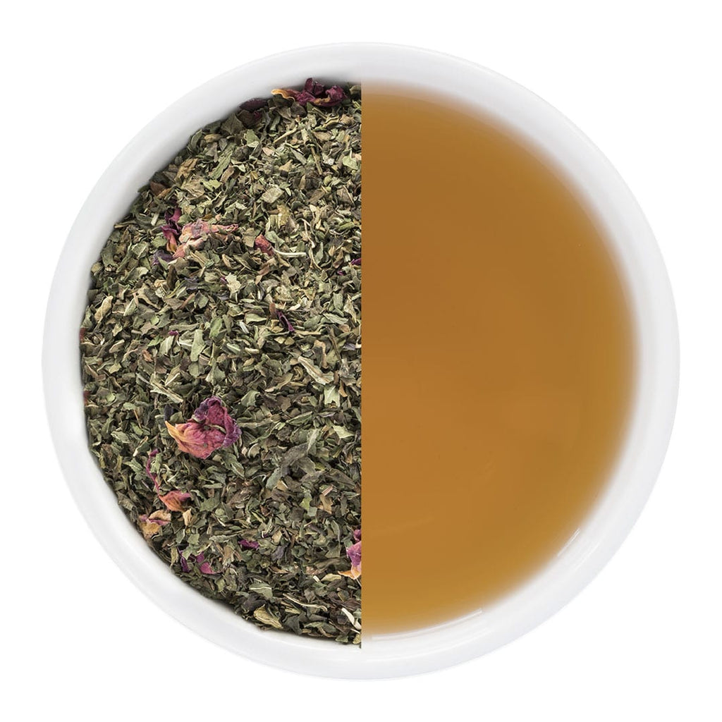 Dried mint leaves and rose petals on one side and brewed tea on the other in a white bowl