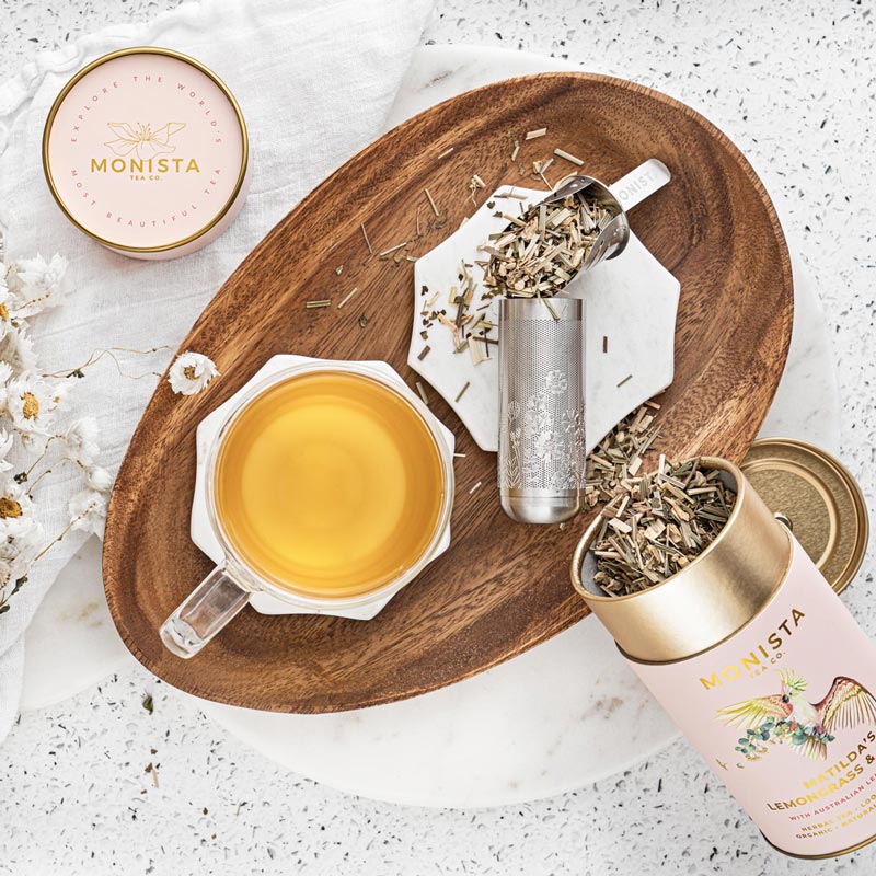 Silver stick tea infuser with loose tea leaves, a cup of brewed tea, and a canister on a wooden tray