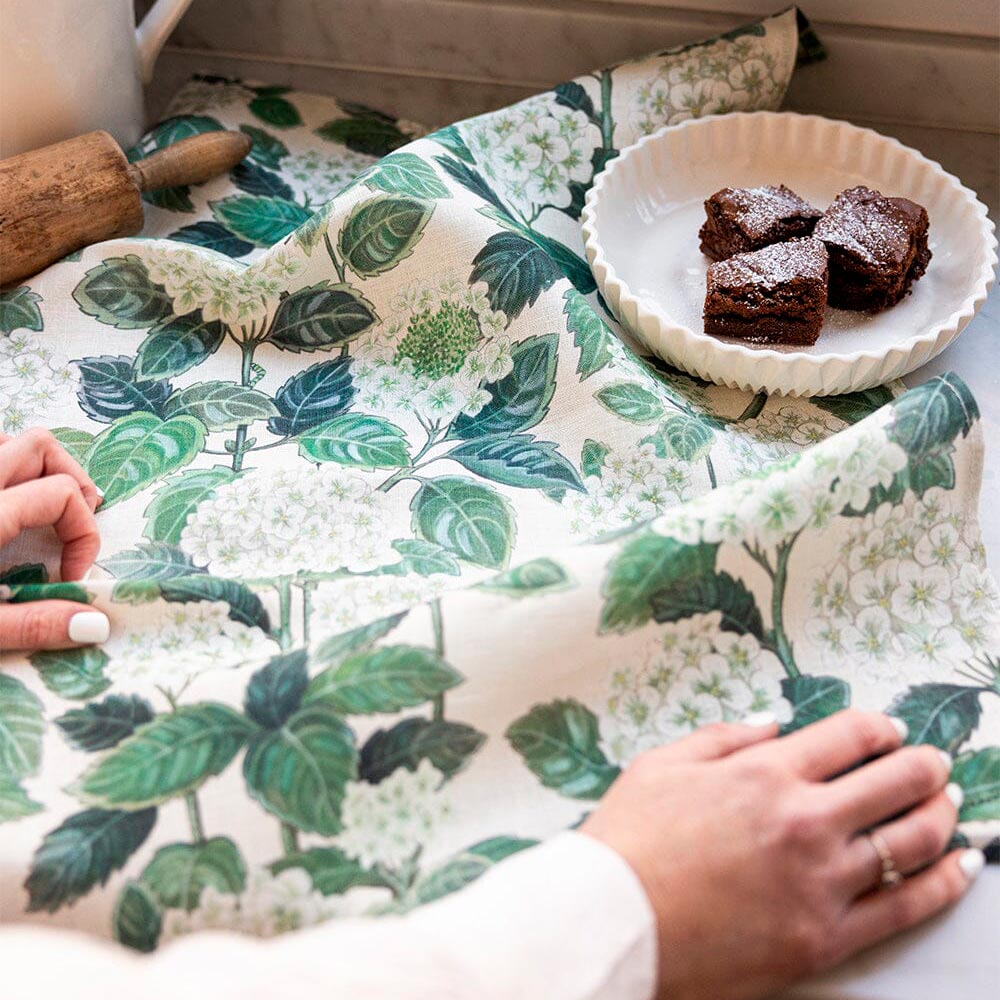 Hydrangea print tea towel on a marble counter with a rolling pin and a plate of brownies