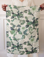 Woman holding up a linen tea towel printed with hydrangeas and green leaves