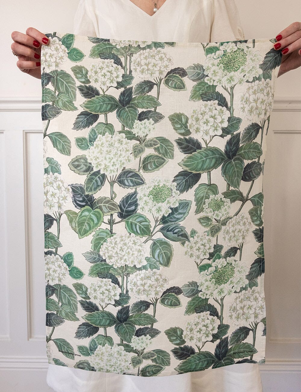 Woman holding up a linen tea towel printed with hydrangeas and green leaves