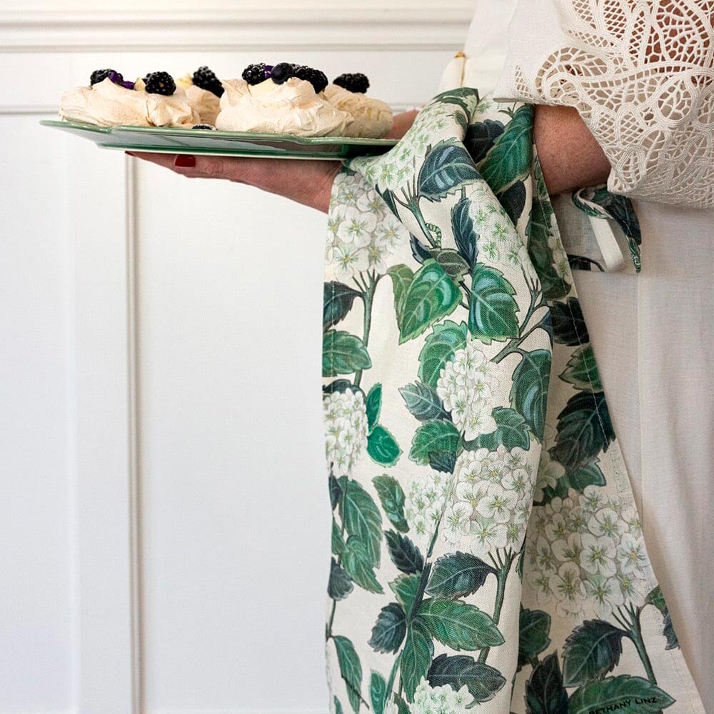 Woman carrying a plate of pavlovas with a hydrangea print tea towel draped over her arm