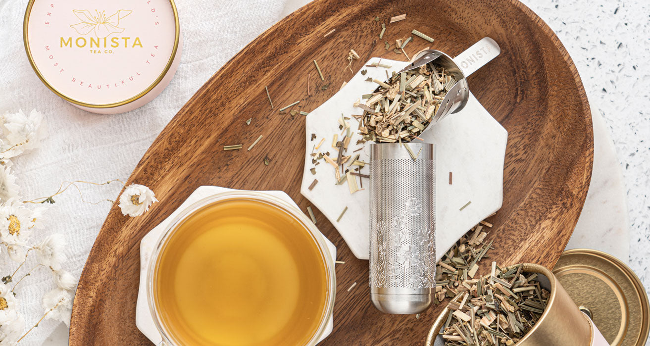 Tea-making setup with a wooden tray, tea leaves, a teacup of brewed tea, and a container of loose tea.