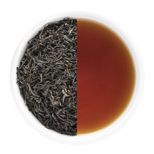 Tea leaves on one side and brewed tea on the other in a white bowl