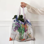 Woman carrying leafy greens in a reusable shopping bag printed with a cockatoo and flowers