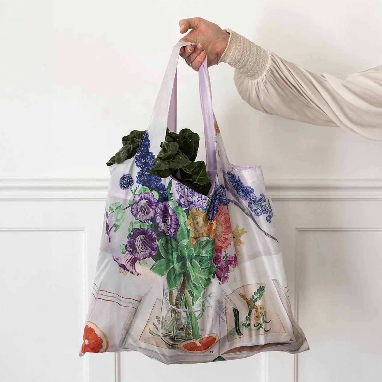 Woman carrying leafy greens in a reusable shopping bag printed with a cockatoo and flowers