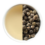 Brewed tea on one side and rolled jasmine pearl tea leaves on the other in a white bowl